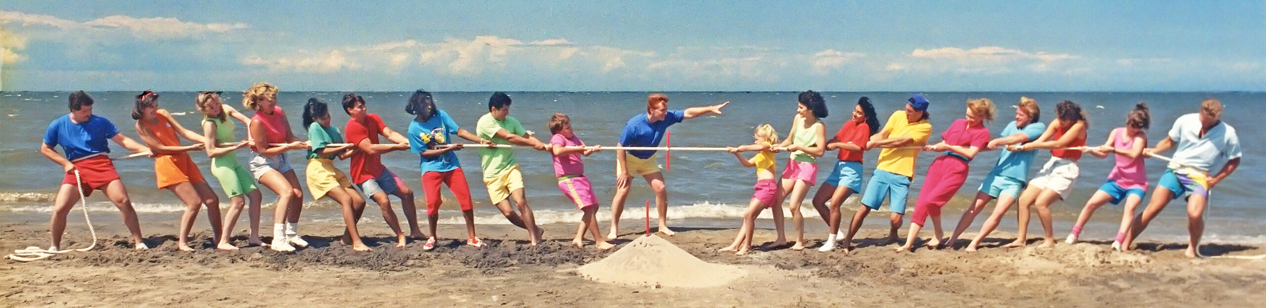 A group of people play tug of war on a beach. A referee stands in the middle.